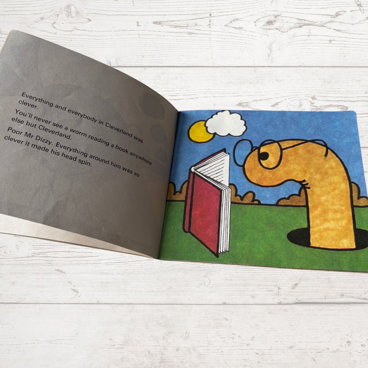 Open book with a cartoon worm reading a book on a wooden surface