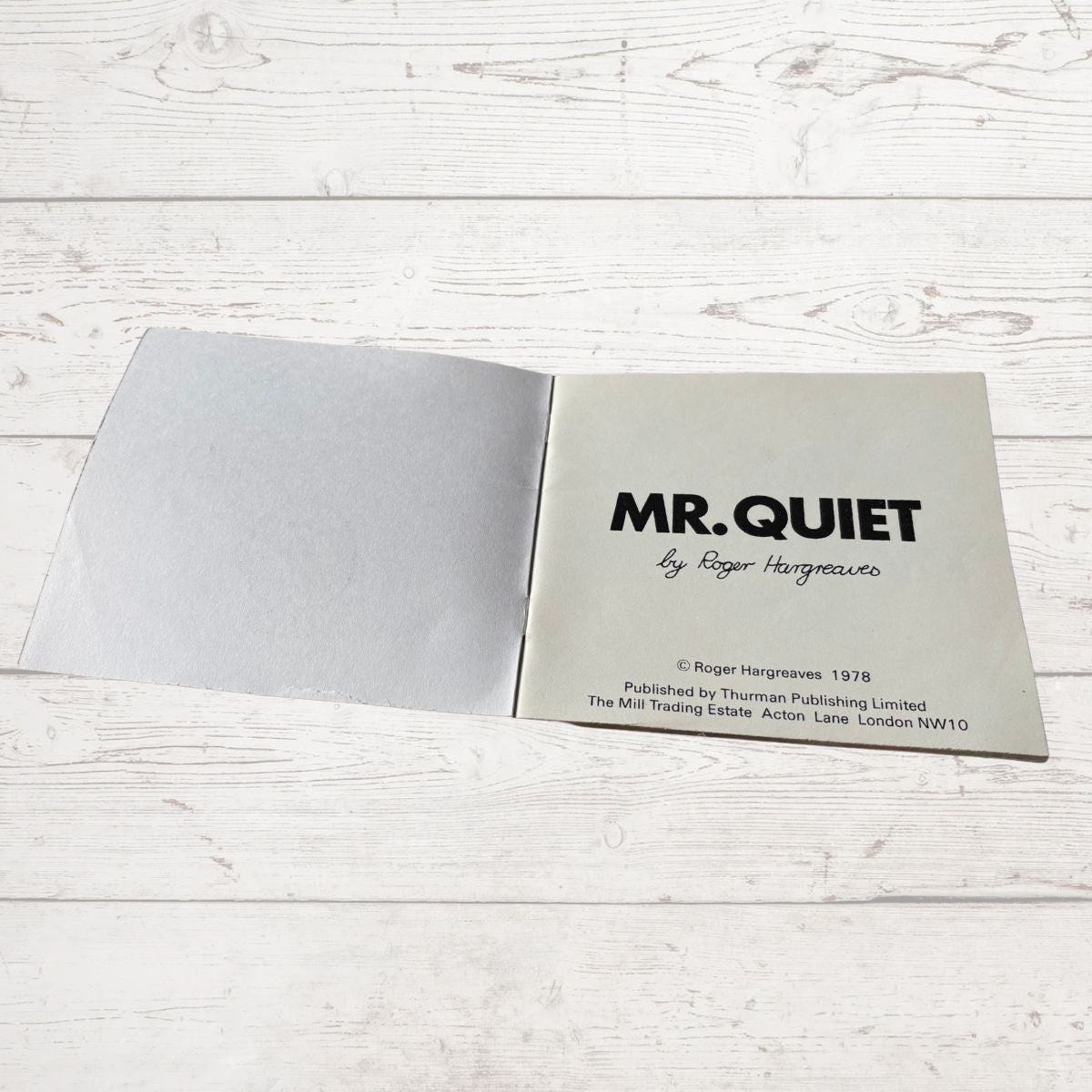 Open book titled 'MR. QUIET' by Roger Hargreaves on a light wooden surface.
