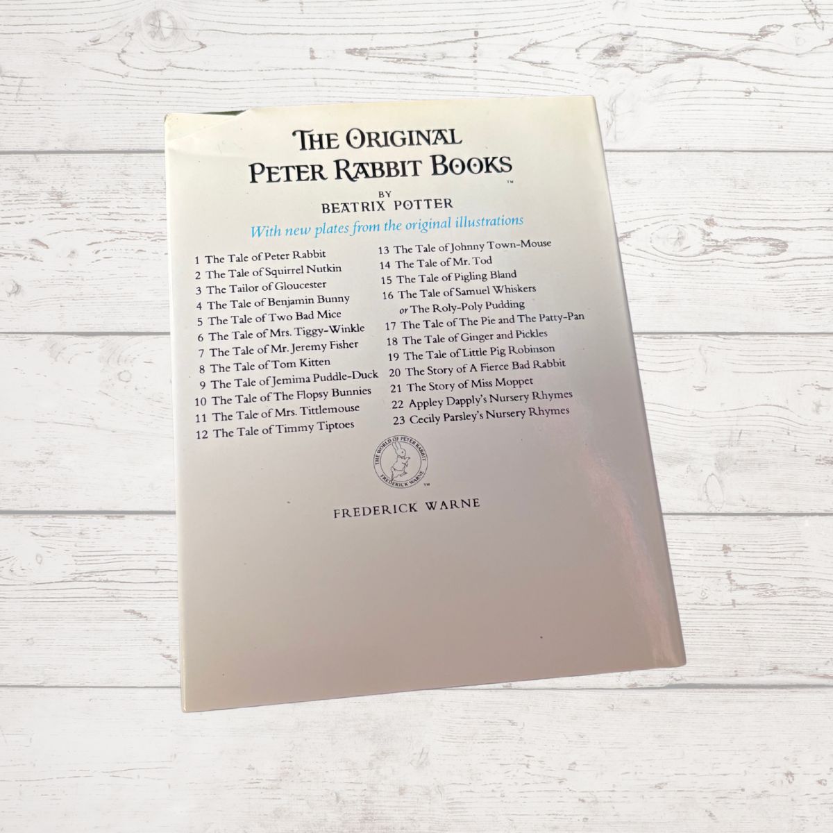 Back cover of a book titled 'The Original Peter Rabbit Books' by Beatrix Potter on a light wooden surface.