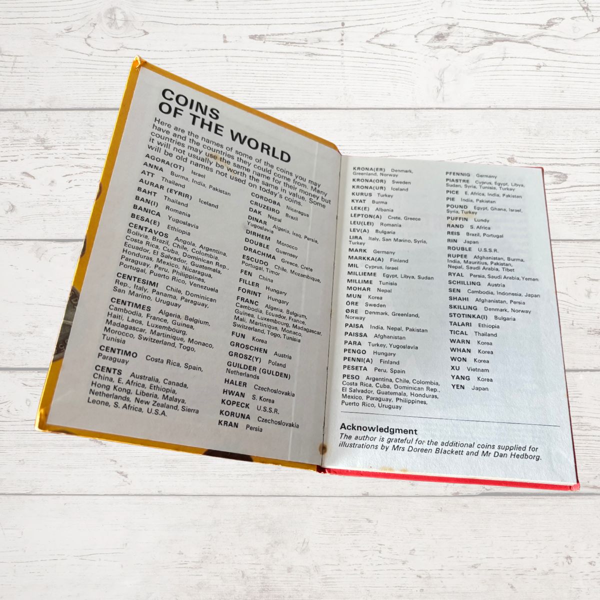 Open book showing a list of coins from around the world on a wooden surface.