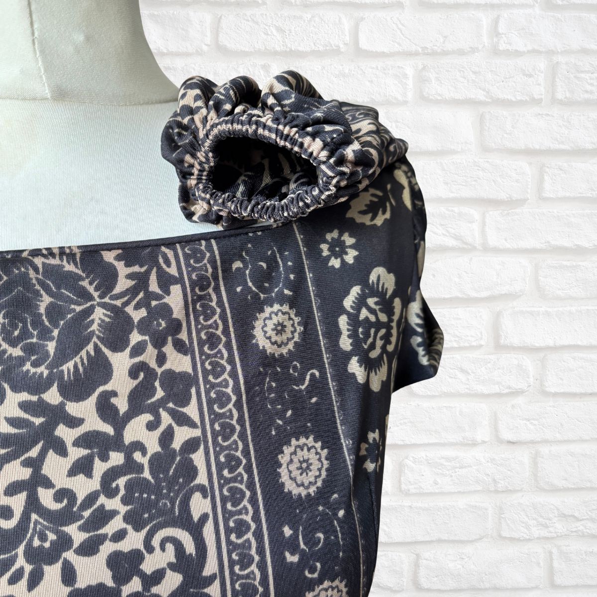 Black and white patterned fabric draped over a mannequin against a white brick wall.