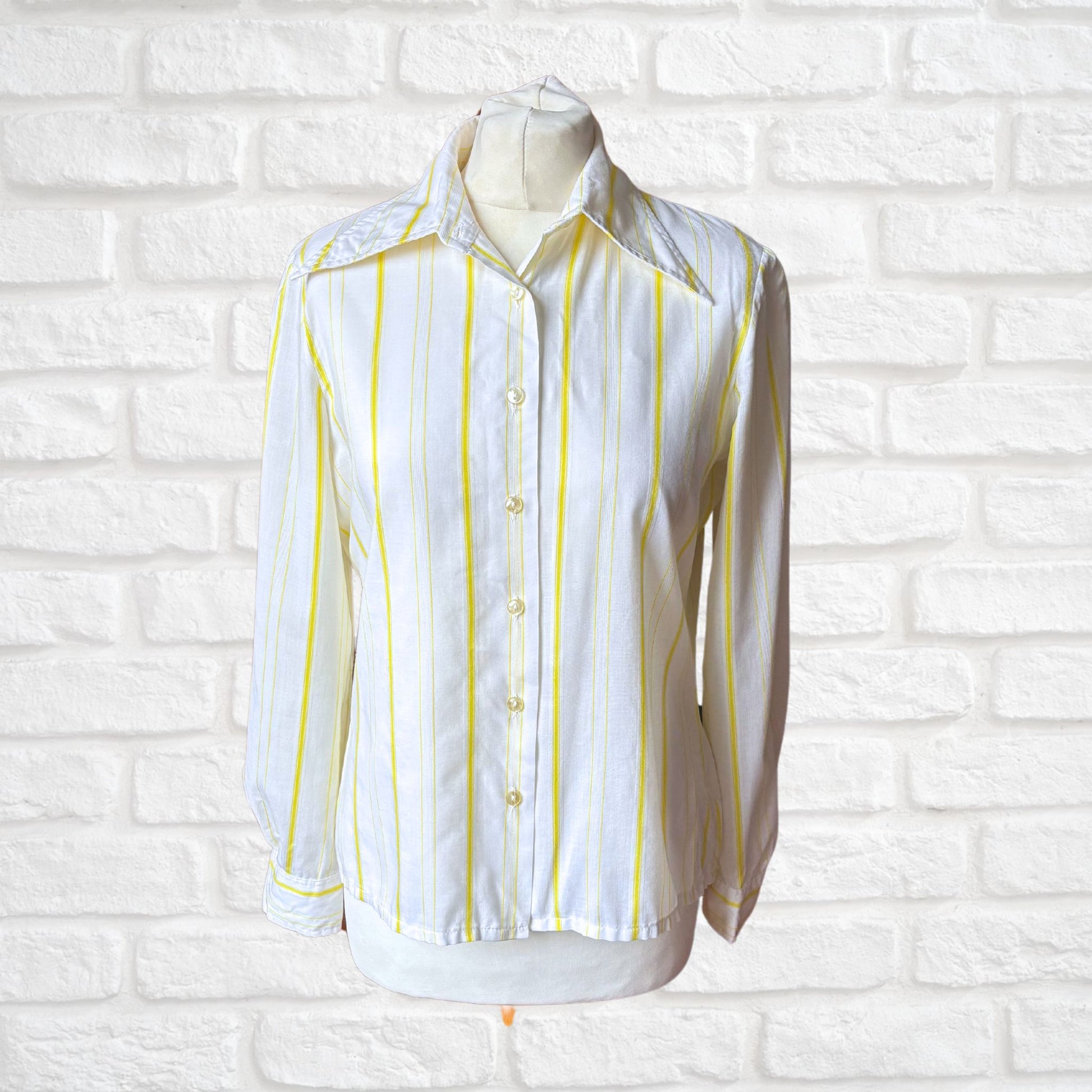 A vintage 1970s white cotton blend shirt with yellow stripes, displayed on a mannequin against a white brick wall.