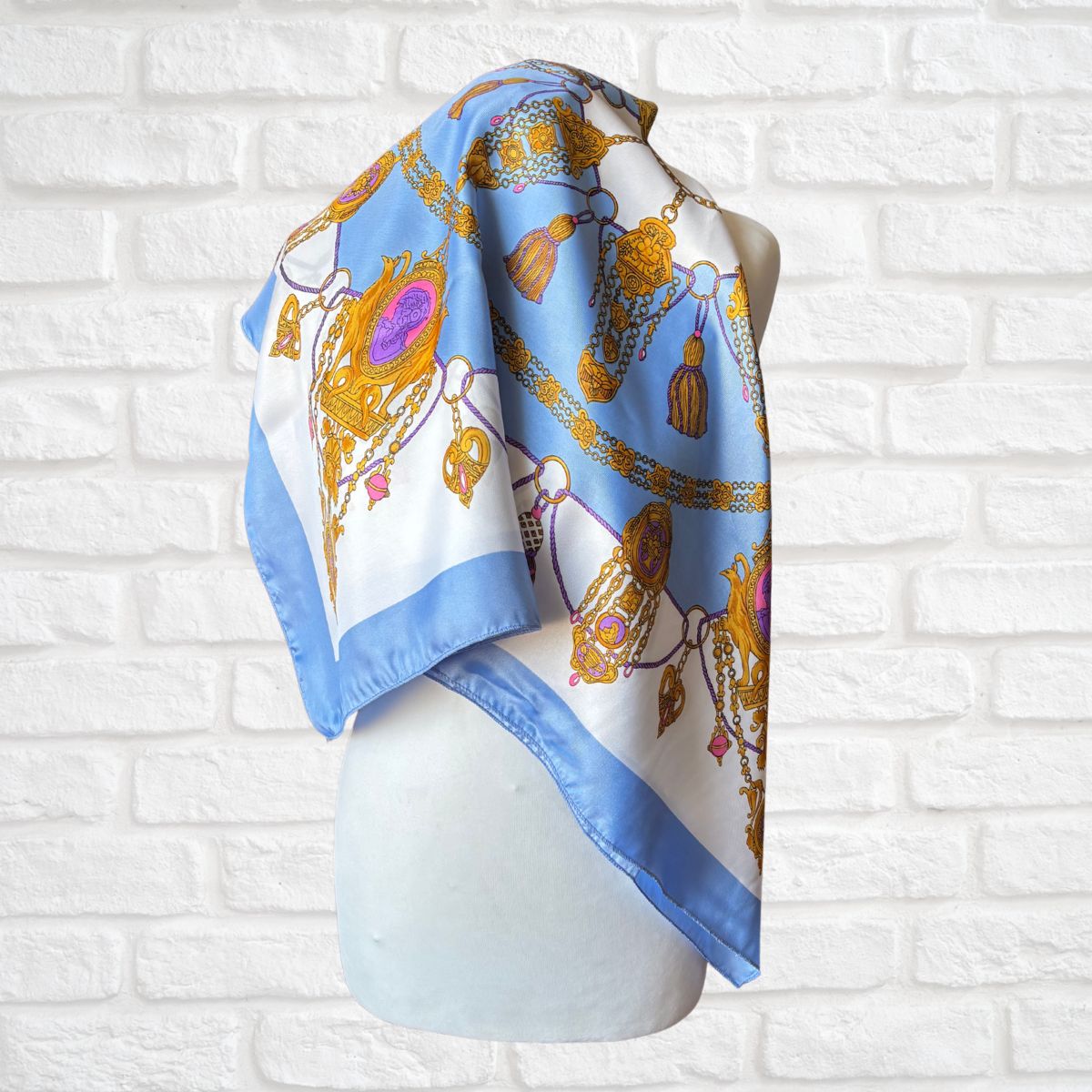 Decorative scarf with gold and blue patterns on a mannequin against a white brick wall.