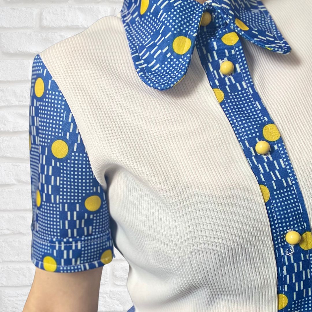 A white  60s mod dress with rounded blue and yellow spotted collar, front placket and sleeves. Yellow button fastening.