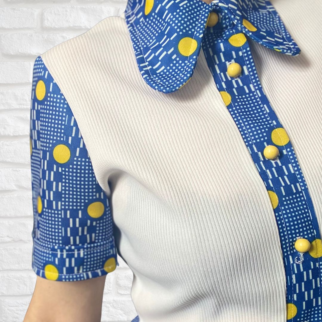 A white  60s mod dress with rounded blue and yellow spotted collar, front placket and sleeves. Yellow button fastening. 