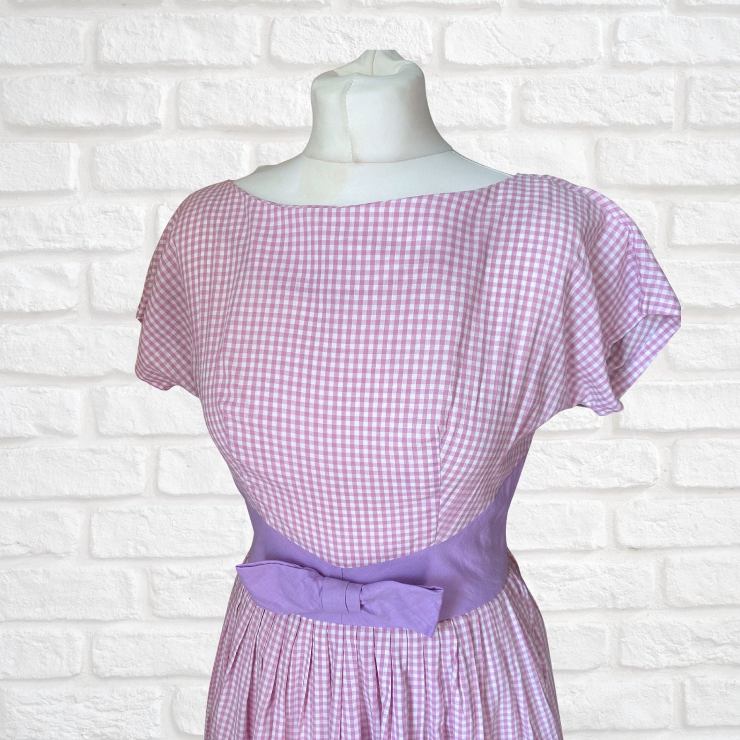 A lilac and white cotton gingham 1950s dress with short sleeves and a mauve bow at the waist