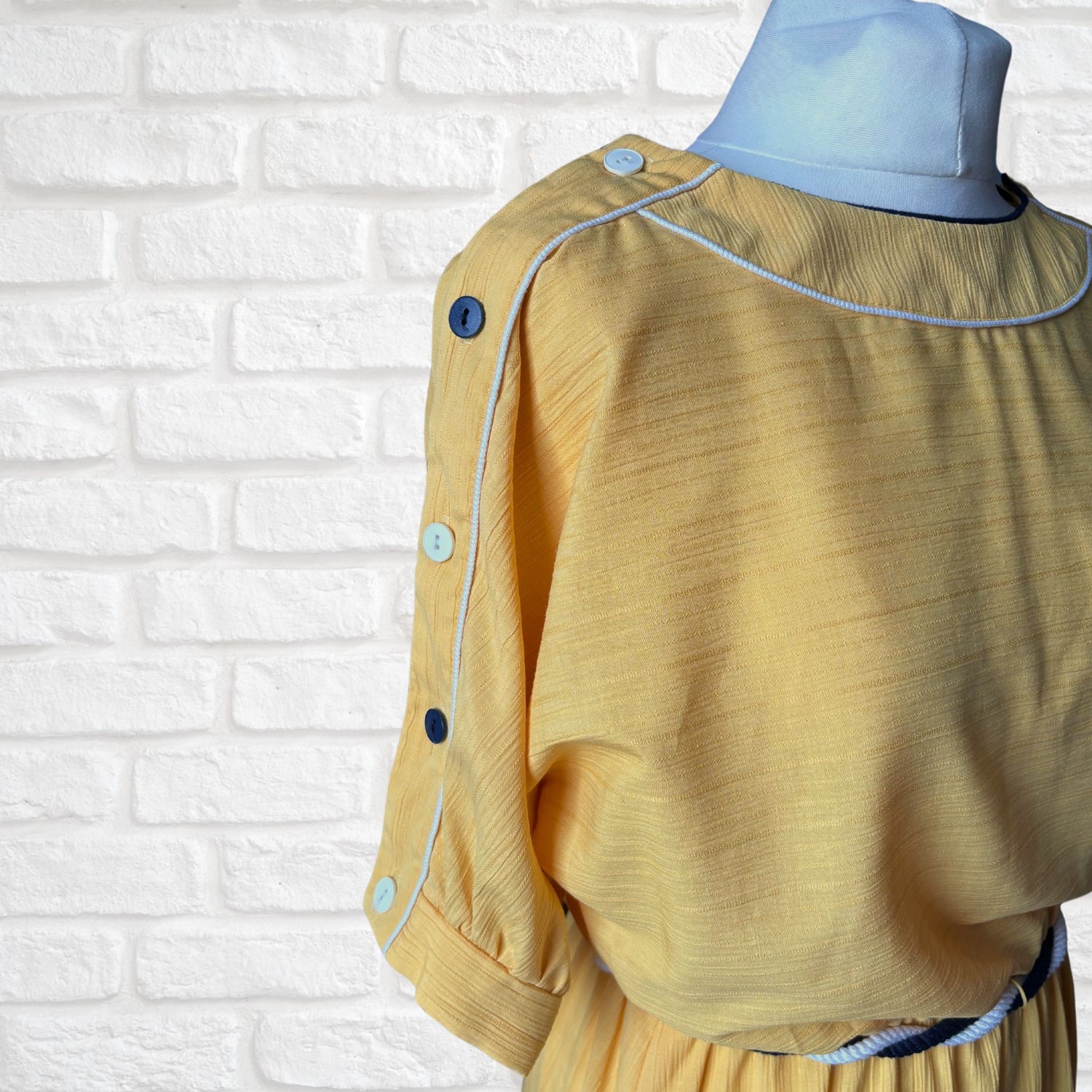 A yellow 80s dress with navy and white button detailing on the sleeve 