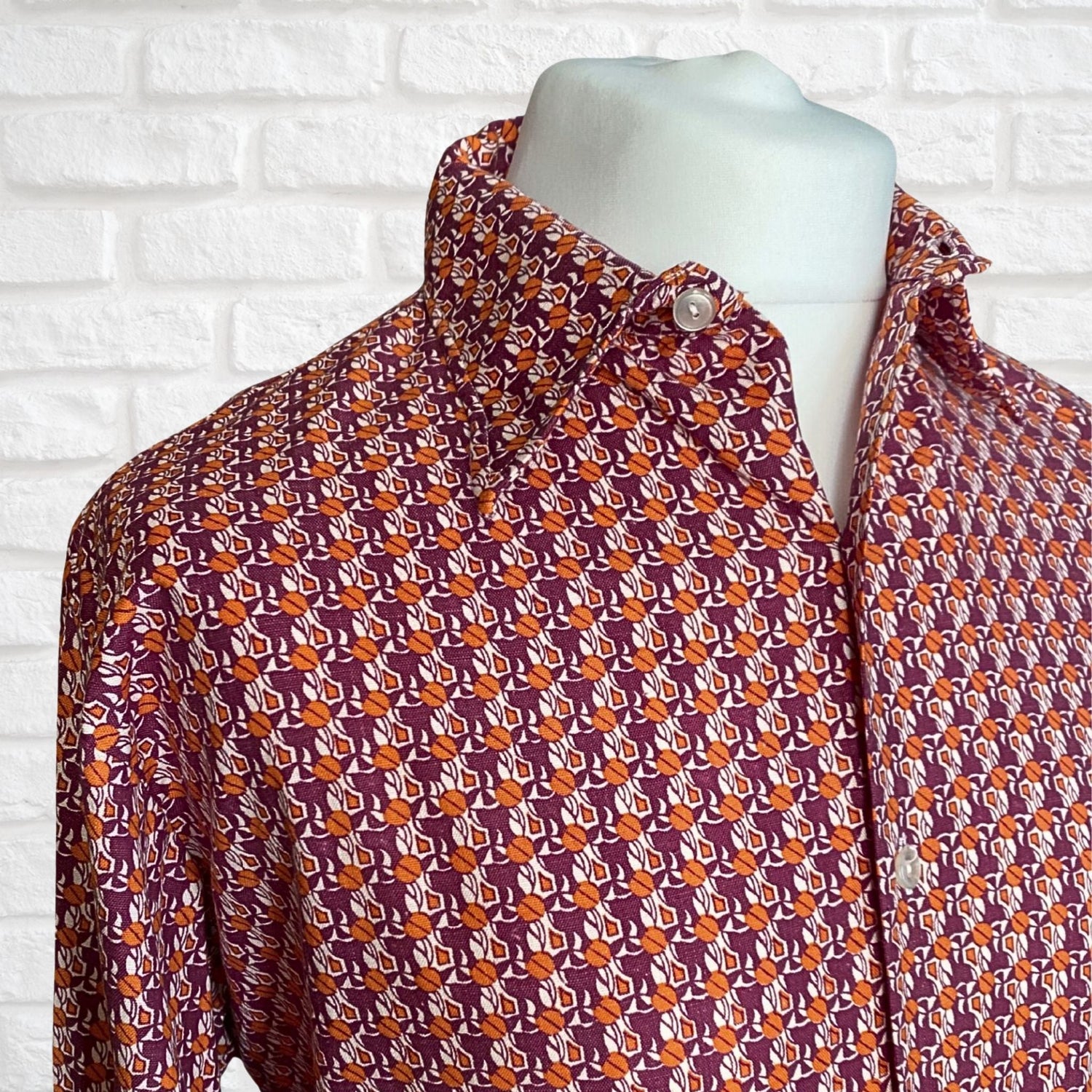 A close up image of a 1970s orange and purple abstract print vintage men’s shirt