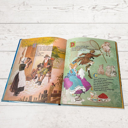 An open children's book with illustrated pages, photographed flat on a white wood surface. The left page shows a colorful historical scene with text, and the right page shows a whimsical scene with text and illustrations.