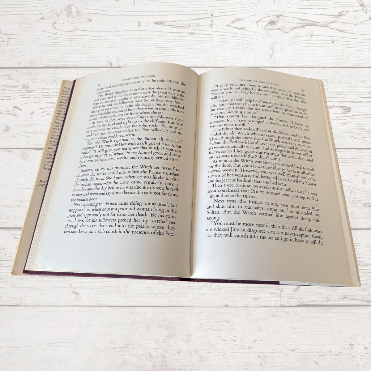 An open vintage book showing printed text on both pages, photographed from above on a light whitewashed wooden surface.