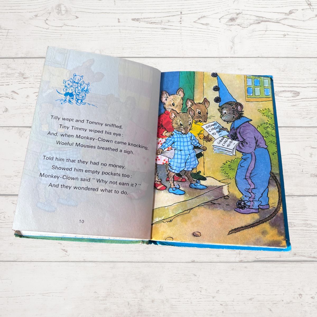 An open children's book lying on a whitewashed wooden surface, showing a printed story with text on the left page and a colorful illustration on the right page.