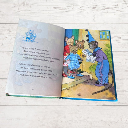 An open children's book lying on a whitewashed wooden surface, showing a printed story with text on the left page and a colorful illustration on the right page.
