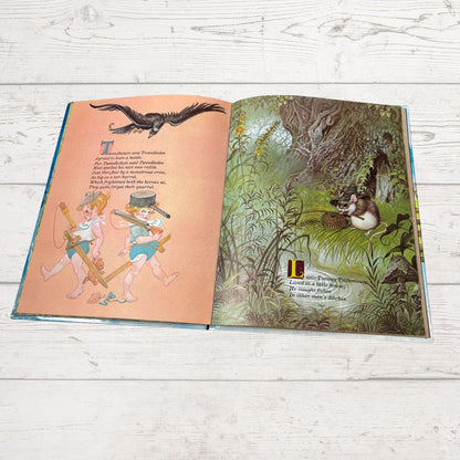 An open children's picture book spread on a white wood surface, showing illustrated pages with text and colorful drawings of animals in a forest scene.