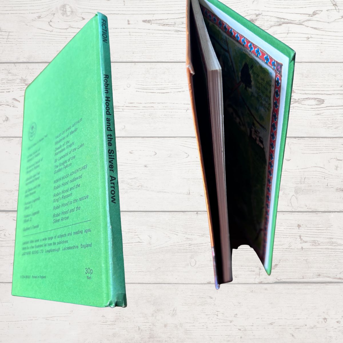 A hardcover book titled 'Robin Hood and the Silver Arrow' shown from two angles on a light wood background. One view shows the mint green back cover with printed text, and the other shows the open interior pages with a colorful border and green-toned illustration.