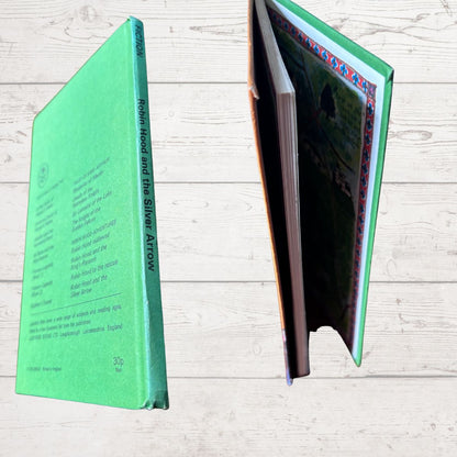 A hardcover book titled 'Robin Hood and the Silver Arrow' shown from two angles on a light wood background. One view shows the mint green back cover with printed text, and the other shows the open interior pages with a colorful border and green-toned illustration.