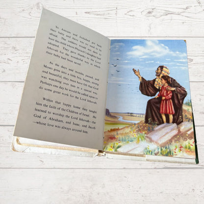 Open book with a illustrated page of a man and child standing on a mountain, on a light wooden surface.