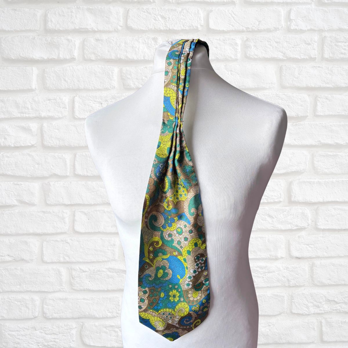 Colorful paisley-patterned tie on a mannequin against a white brick wall.