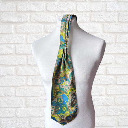 Colorful paisley-patterned tie on a mannequin against a white brick wall.