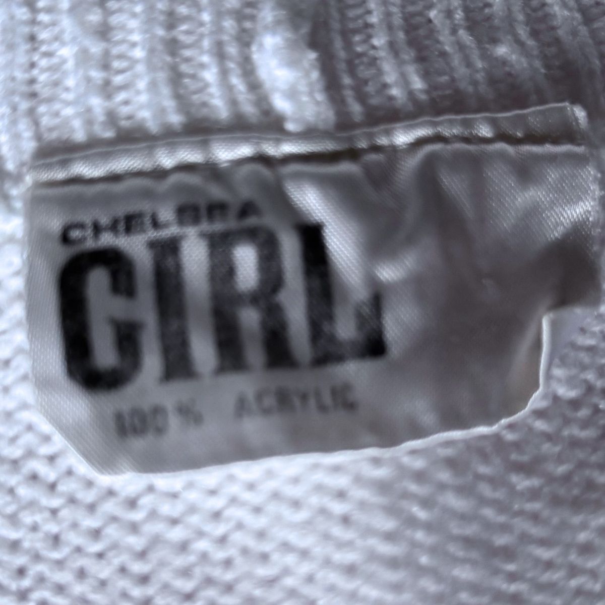Close-up of a white textured fabric tag with black text reading 'CHELSEA GIRL' and '100% ACRYLIC'.