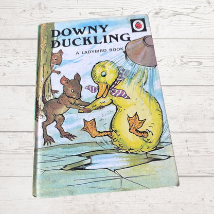 Vintage book titled 'Downy Duckling' by Ladybird, featuring a colourful illustration of a yellow duckling in the rain with a squirrel on a light wood background.