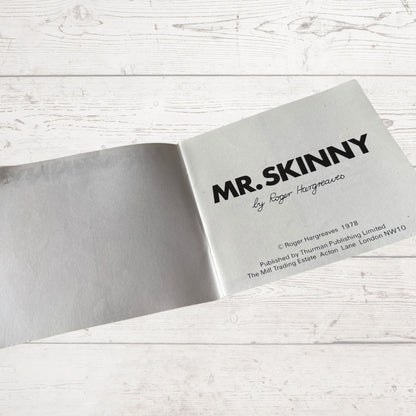 Open book with 'MR. SKINNY' title on a light wooden surface