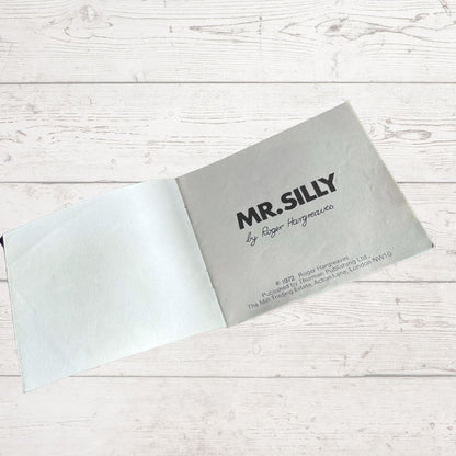 Gray book titled 'MR. SILLY' by Roger Hargreaves on a light wooden surface