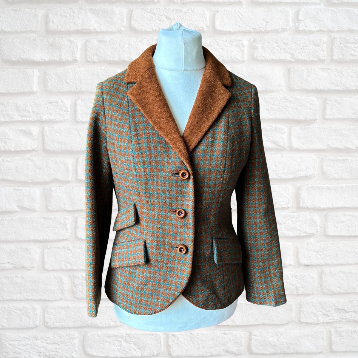 Plaid blazer with brown collar on a mannequin against a white brick wall.