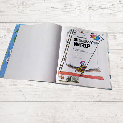 Open book titled 'Busy, Busy World' on a wooden surface
