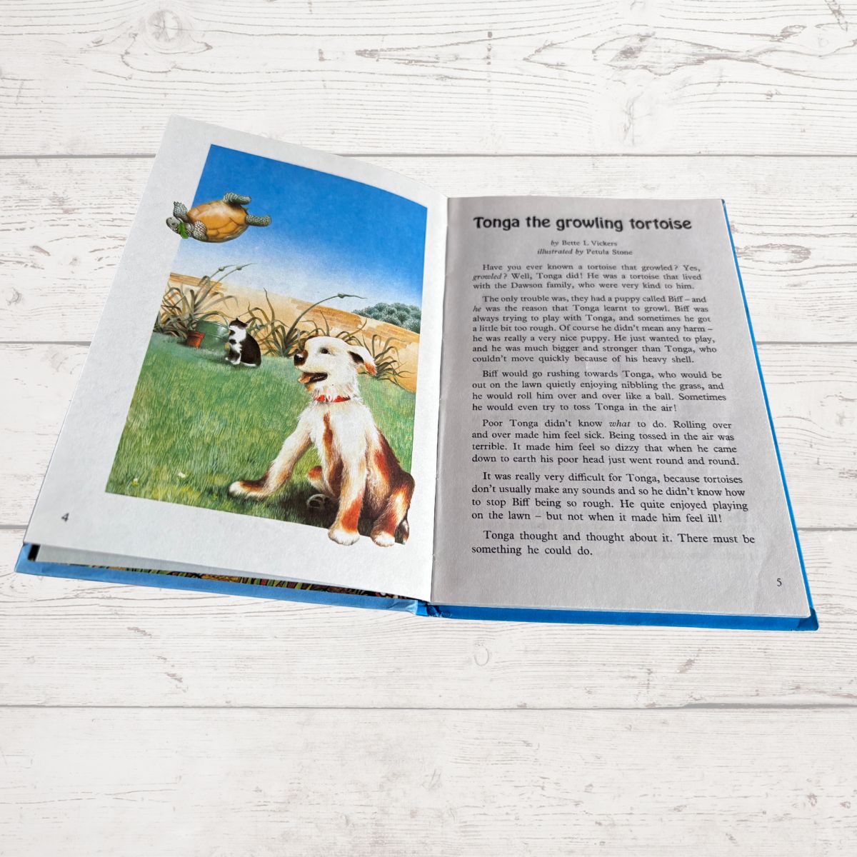 An open children's book titled 'Tonga the growing tortoise' laid flat on a white wooden surface. The left page shows a colorful illustration of a turtle in a grassy landscape, and the right page contains the printed text of the story.