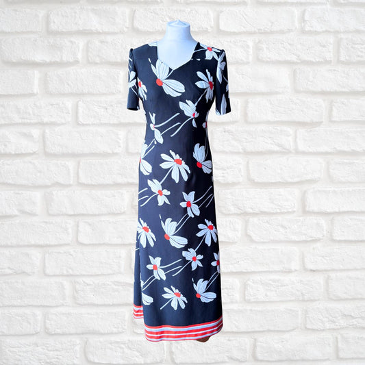 Black dress with floral pattern on a mannequin against a white brick wall.