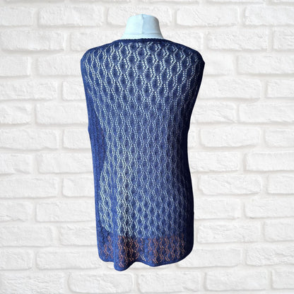A blue open-knit sleeveless cardigan displayed on a white mannequin torso against a white brick wall background.