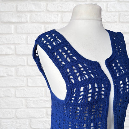A royal blue open-knit crochet vest displayed on a white mannequin torso against a white brick wall background.