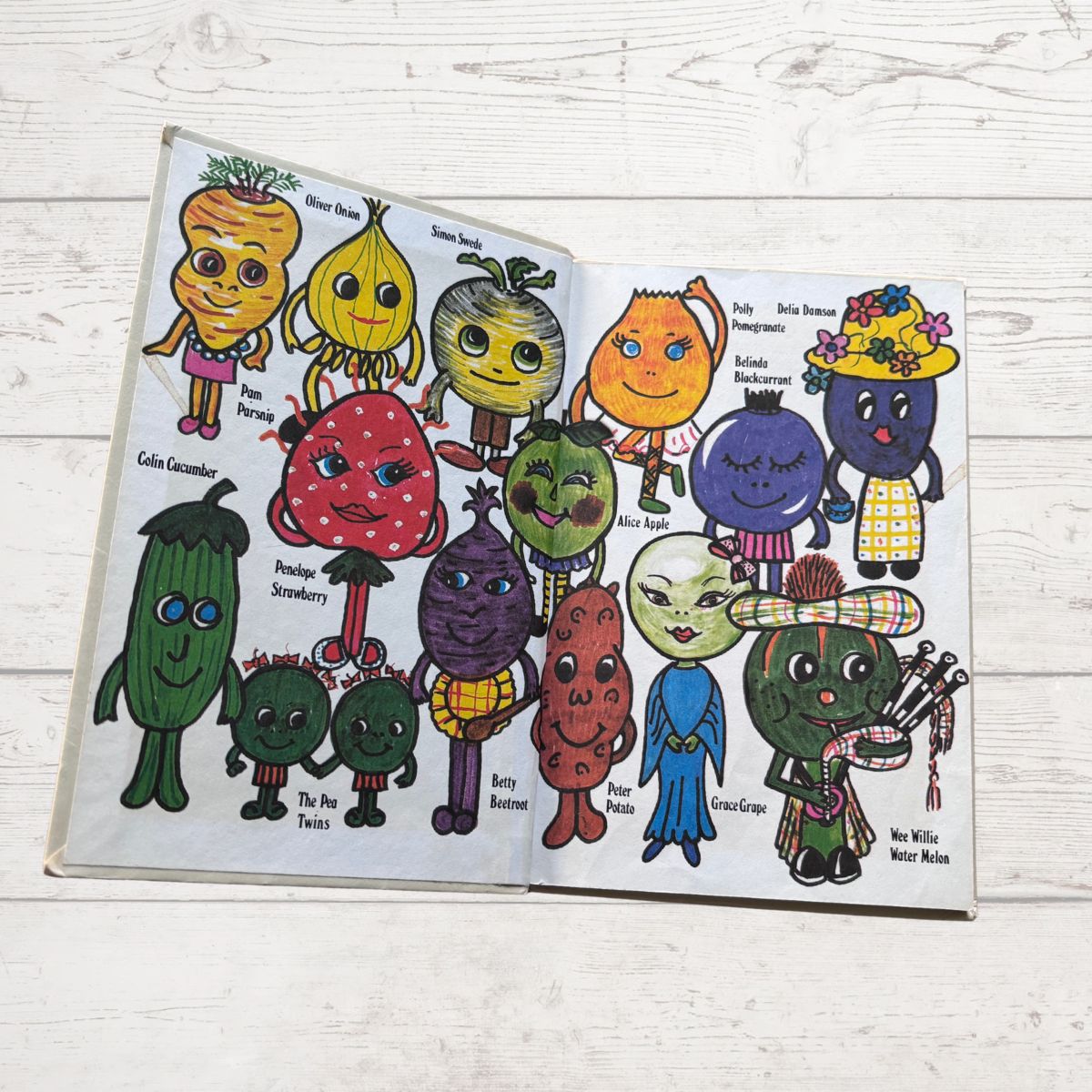 Open book with colorful illustrations of vegetables with faces on a wooden surface