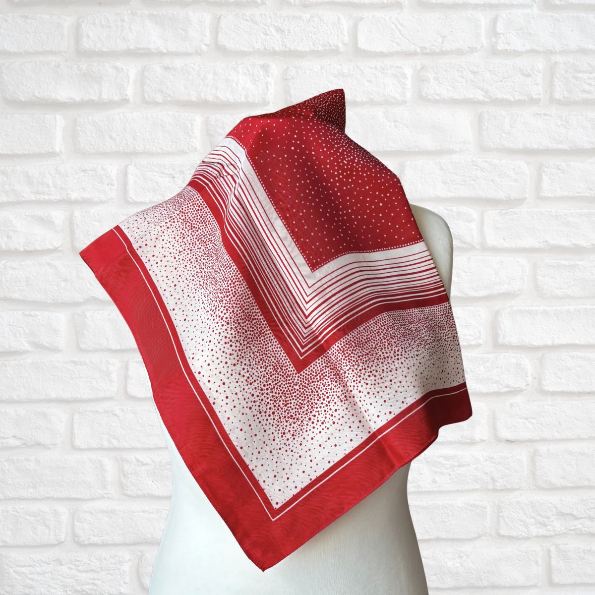 Red and white patterned scarf on a mannequin against a white brick wall background