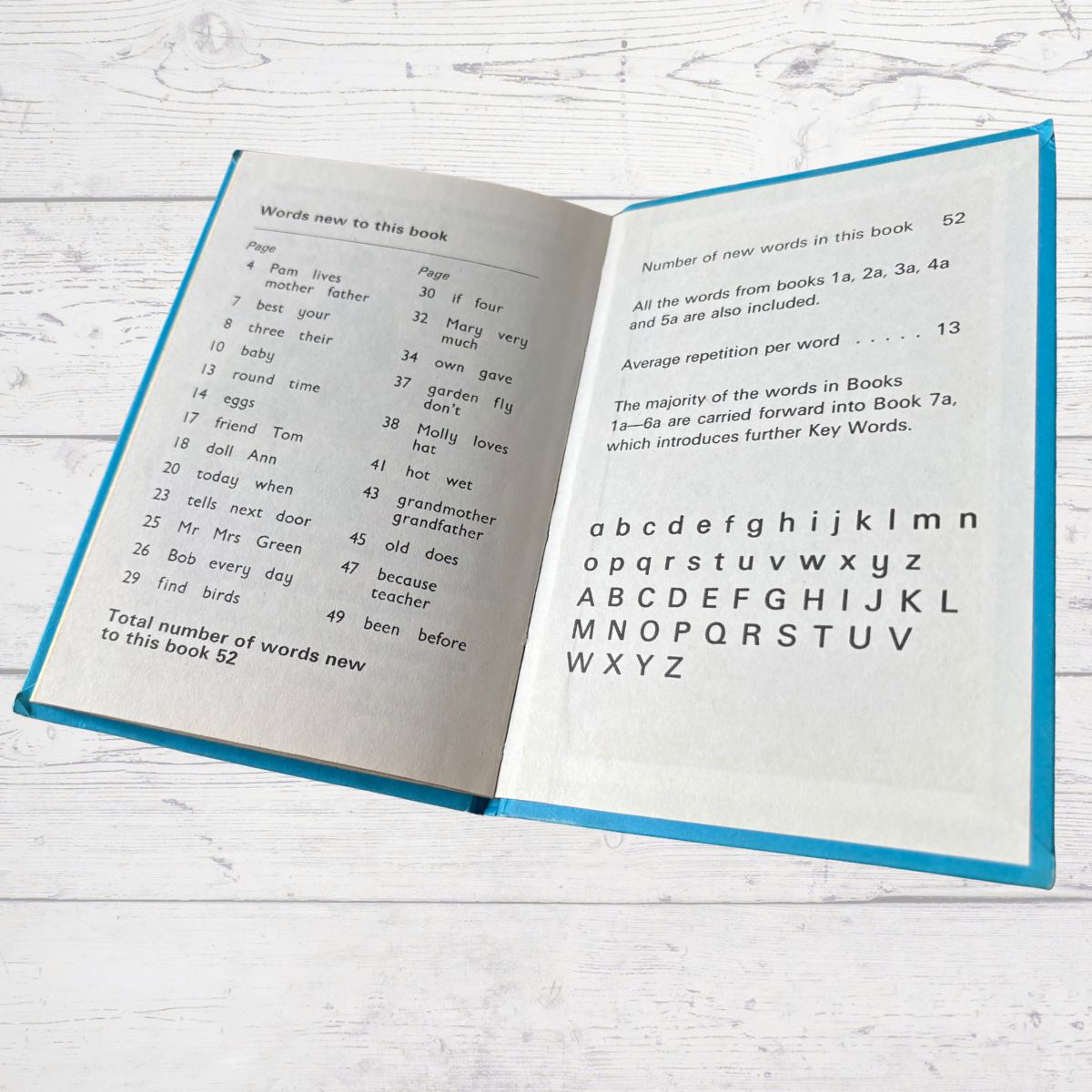 Open book with text and alphabet on a white wooden surface