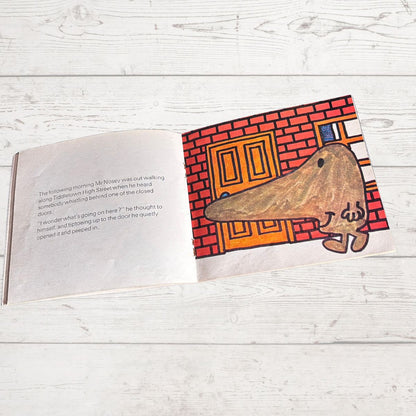 Illustrated book page with a character peeking around a door on a wooden surface
