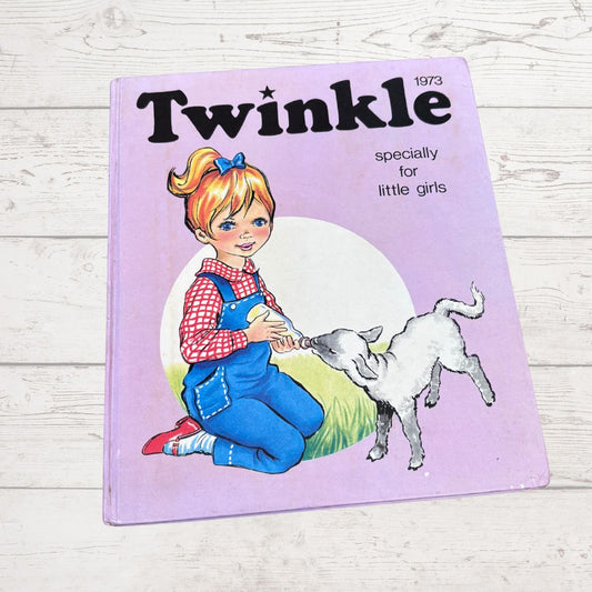 Vintage children's book titled 'Twinkle' with cover art showing a young girl kneeling beside a white goat on a light purple background, photographed on a whitewashed wood surface.