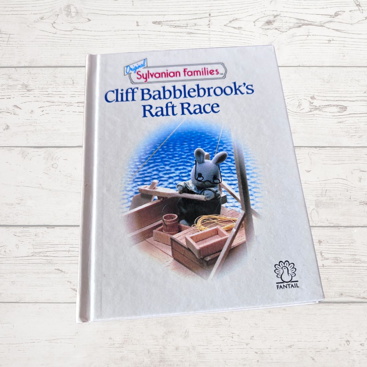 Book titled 'Cliff Babblebrook's Raft Race' from Sylvanian Families on a wooden surface