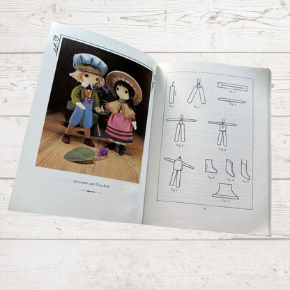 Open book showing illustrations of dolls and their clothing on a wooden surface