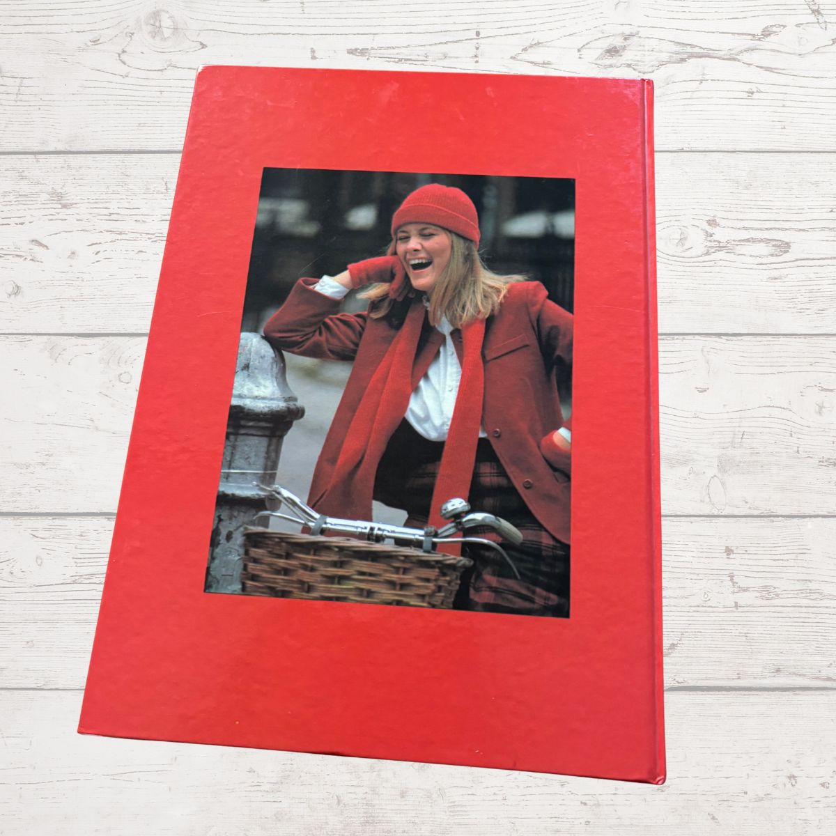 Red photo album with a picture of a woman in a red coat and hat on a wooden surface