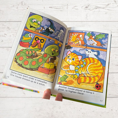 Open children's book with colorful illustrations of a cat and mice on a white wooden surface