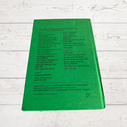 A green book cover by Ladybird Books Ltd, photographed flat on a white wood background. The cover features black printed text listing various children's books and series titles.