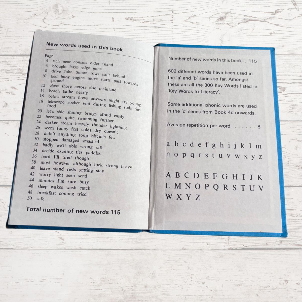 Open book showing text and an alphabet chart on a white wooden surface