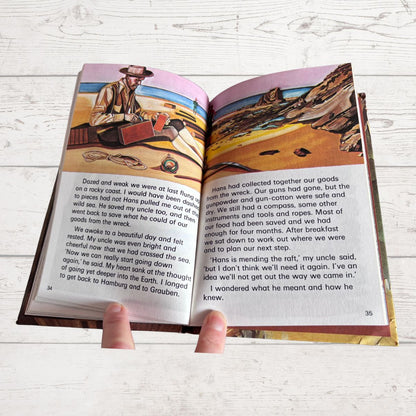 An open children's book spread laid on a light wood surface, showing printed text, illustrations, and a small map on the pages.