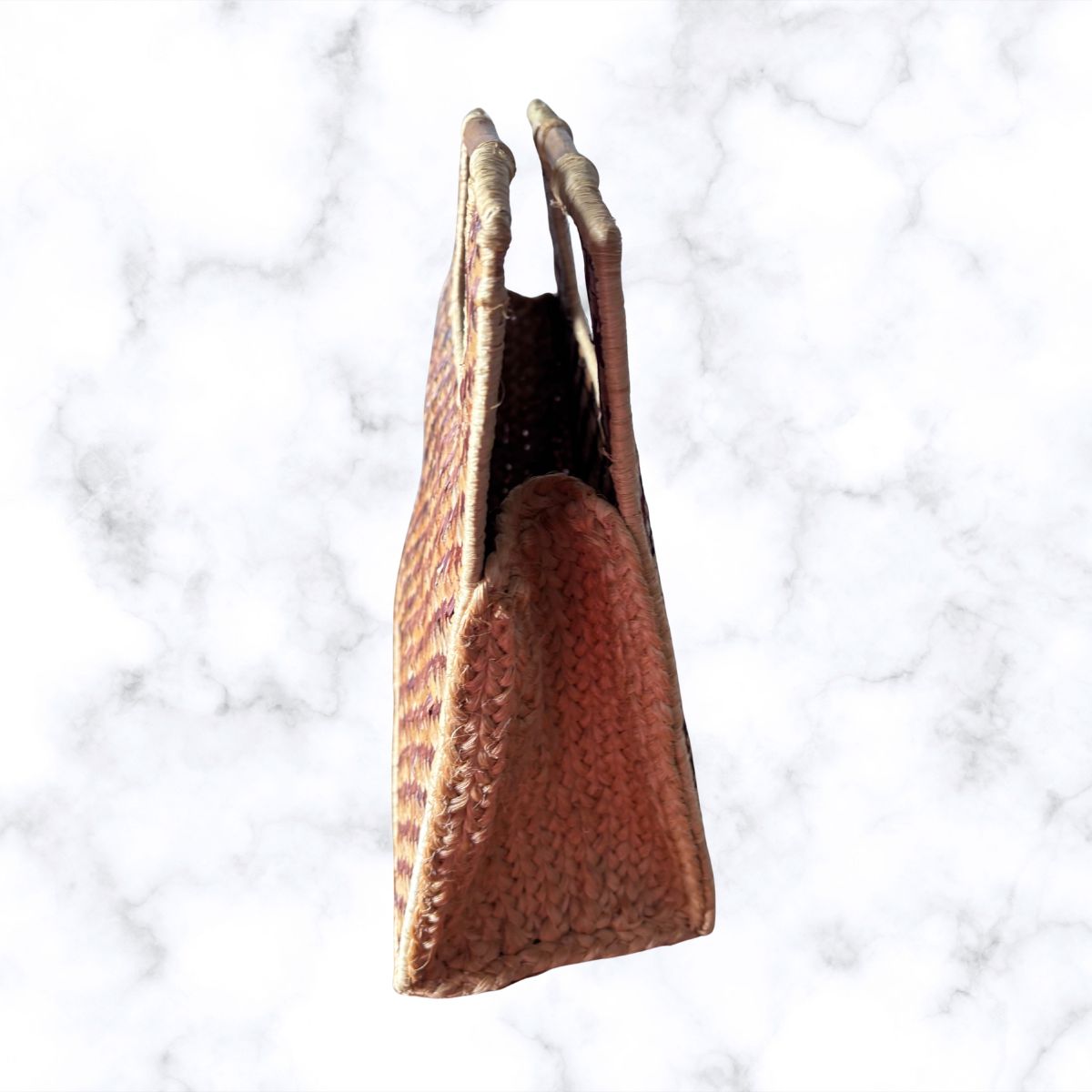 A textured brown woven handbag with an open-top silhouette and top handle shown against a white marble background.
