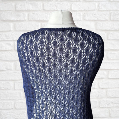 A navy blue open-knit sweater vest displayed on a white mannequin torso, showing a textured diamond lattice pattern against a white brick wall background.