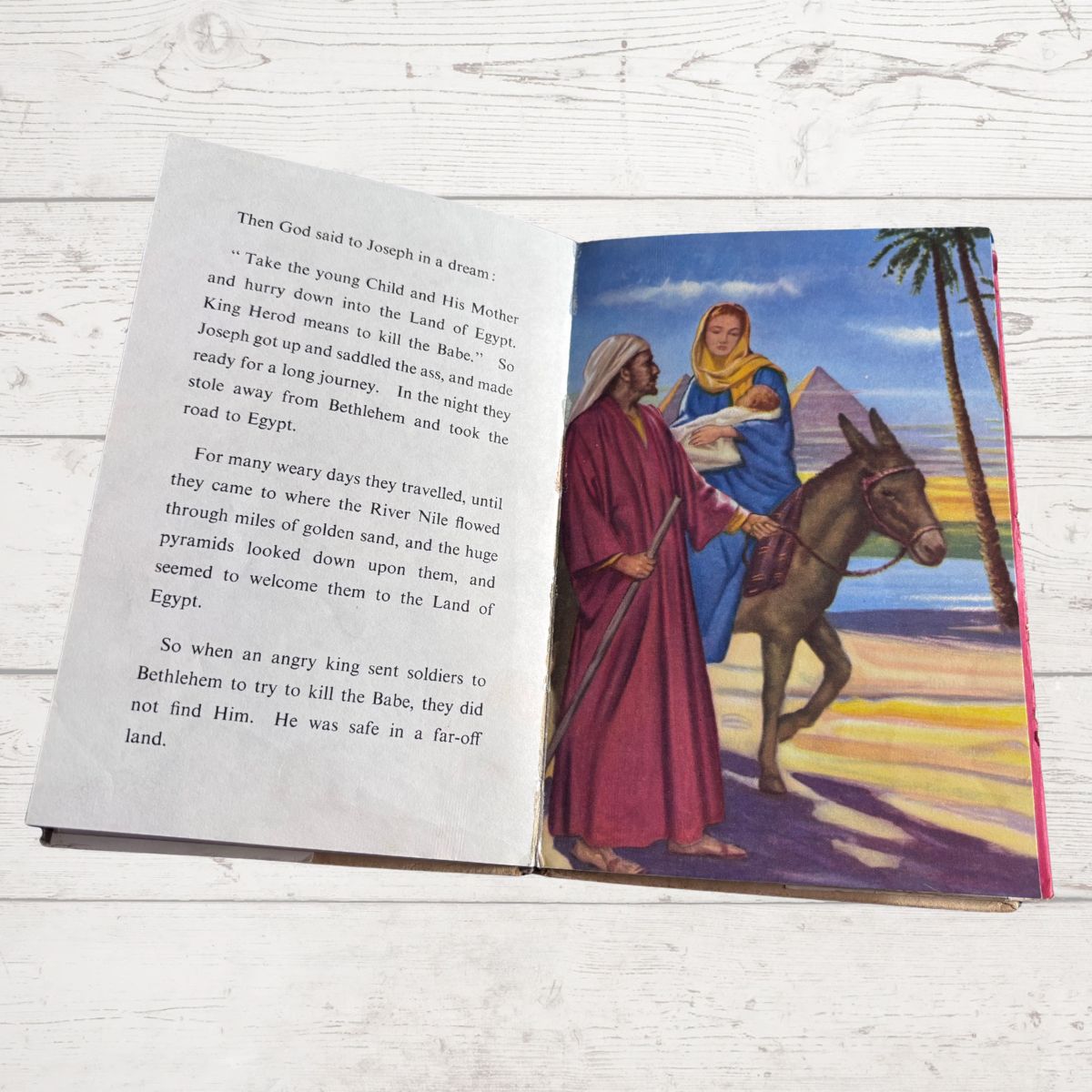 Open book with a colorful illustration of a man and woman with a donkey near pyramids, on a light wooden surface.