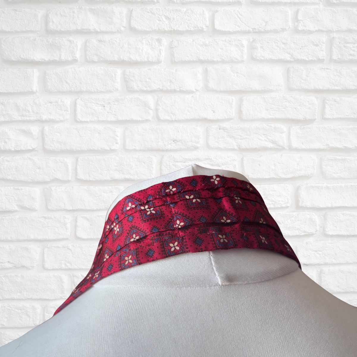 Red patterned cravat on a mannequin against a white brick wall.