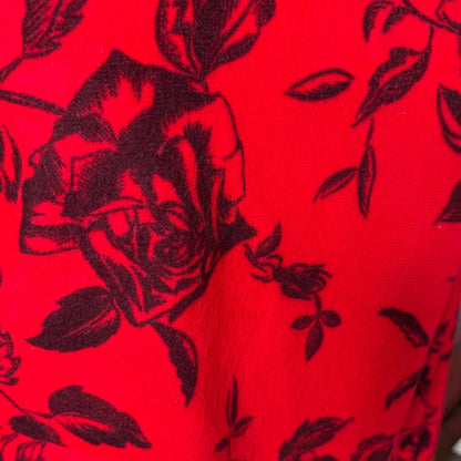 A close-up of a bright red fabric with a black rose and leaf floral pattern.