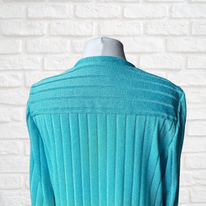 A turquoise ribbed knit cardigan displayed on a mannequin torso against a white brick wall background.